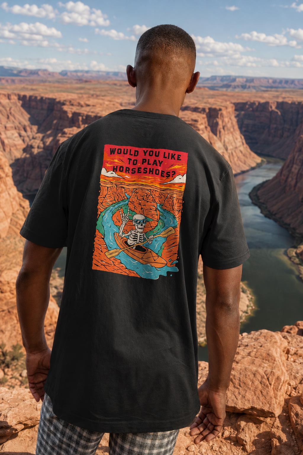 Man wearing a Solid Black Blend Do You Wanna Play Horseshoes? T-shirt with skeleton kayaker back graphic overlooking Horseshoe Bend