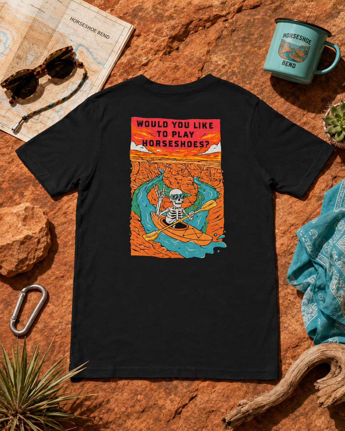 Solid Black Blend Do You Wanna Play Horseshoes? T-shirt featuring the skeleton kayaker Horseshoe Bend back graphic, flat lay with desert hiking gear