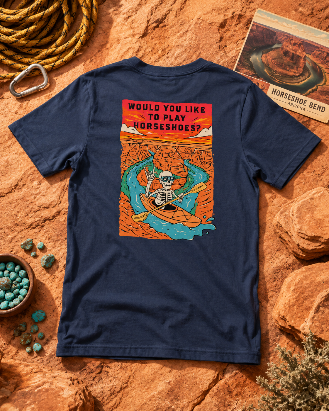 Heather Midnight Navy Do You Wanna Play Horseshoes? T-shirt with skeleton kayaker Horseshoe Bend back graphic, flat lay on red rock with climbing gear