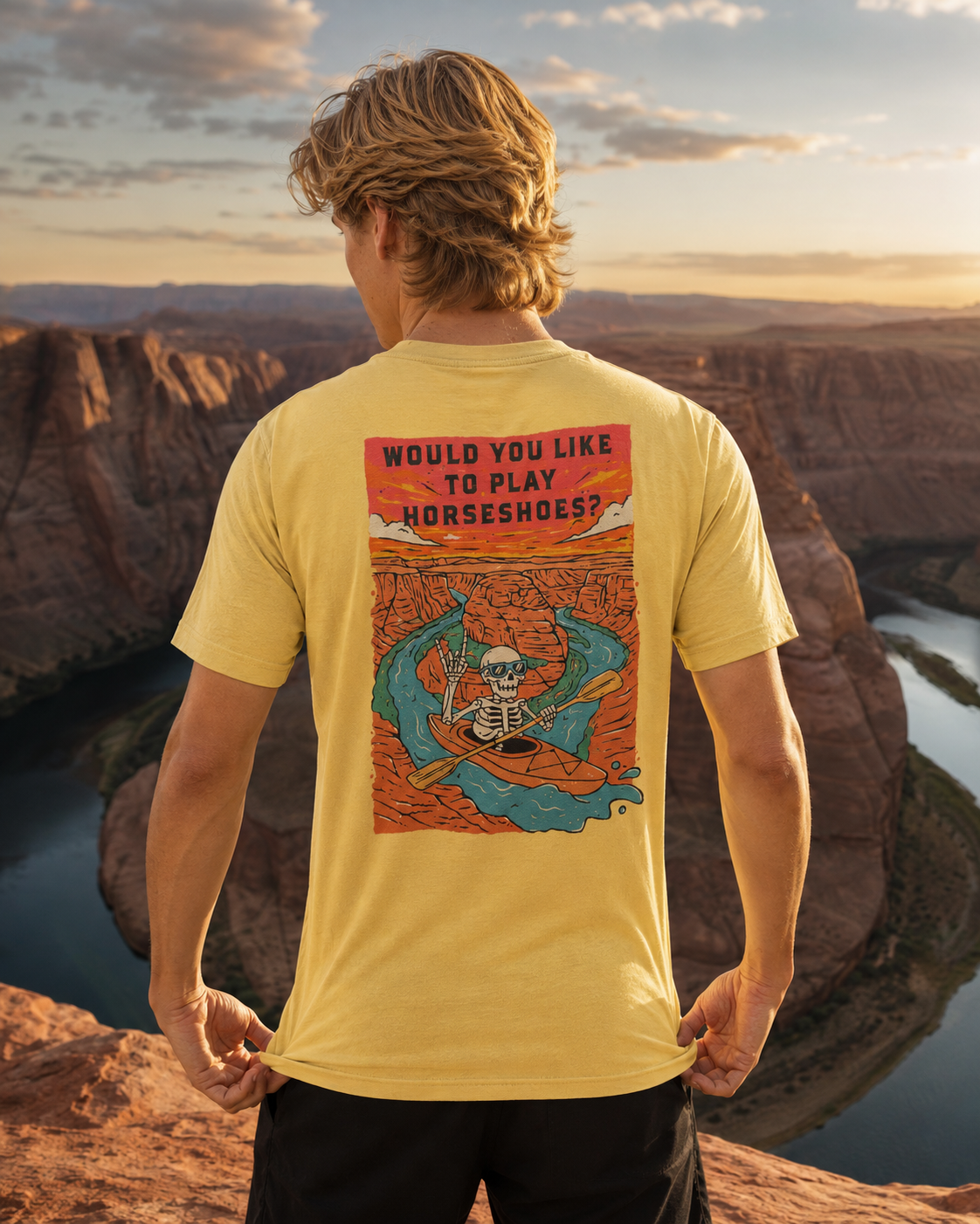 Man wearing a yellow Do You Wanna Play Horseshoes? T-shirt with skeleton kayaker back graphic overlooking Horseshoe Bend