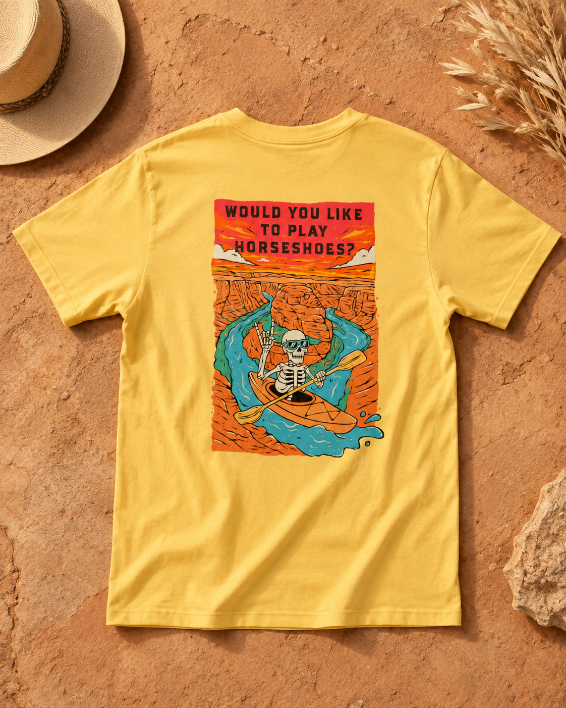 Yellow Do You Wanna Play Horseshoes? T-shirt featuring the skeleton kayaker Horseshoe Bend back graphic, flat lay on desert rock