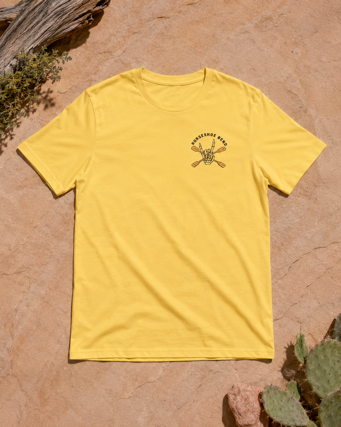 Yellow Gold Do You Wanna Play Horseshoes? T-shirt with small skeleton kayaker chest graphic, flat lay on desert rock