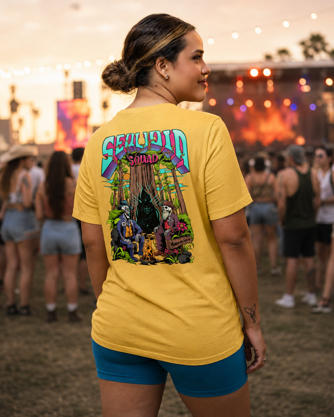 Woman wearing a Heather Yellow Sequoia Squad T-shirt featuring the Mariposa Grove skeleton campfire graphic at a live concert