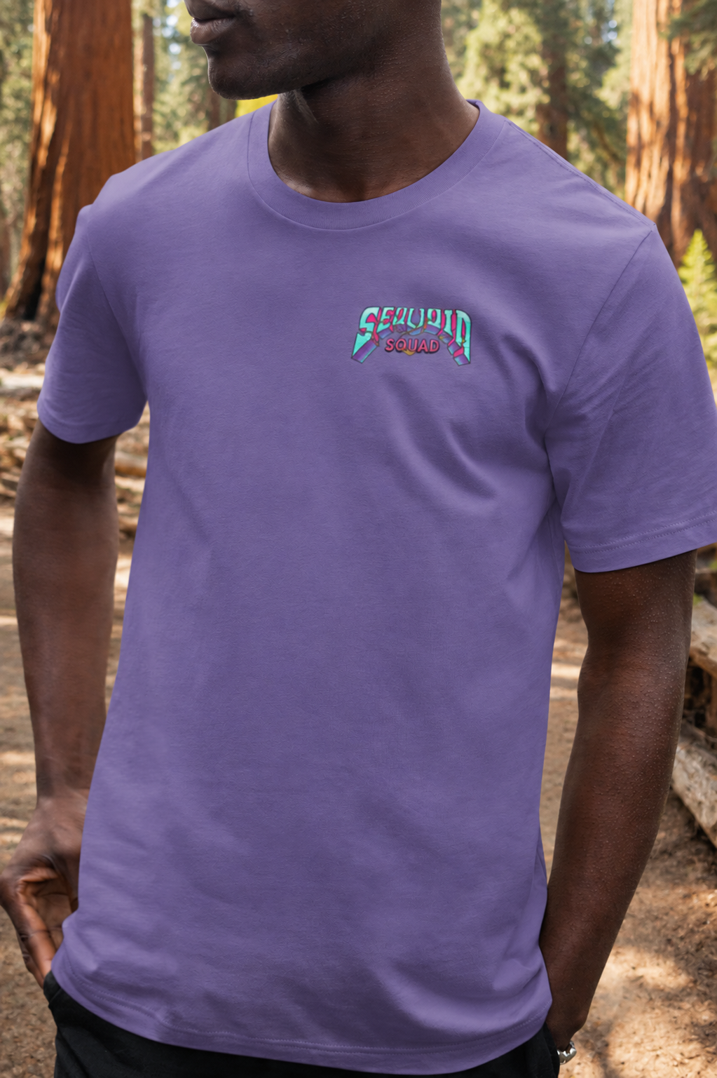 Man wearing a Heather Team Purple Sequoia Squad T-shirt featuring the Mariposa Grove skeleton campfire graphic among the giant sequoias in Mariposa Grove