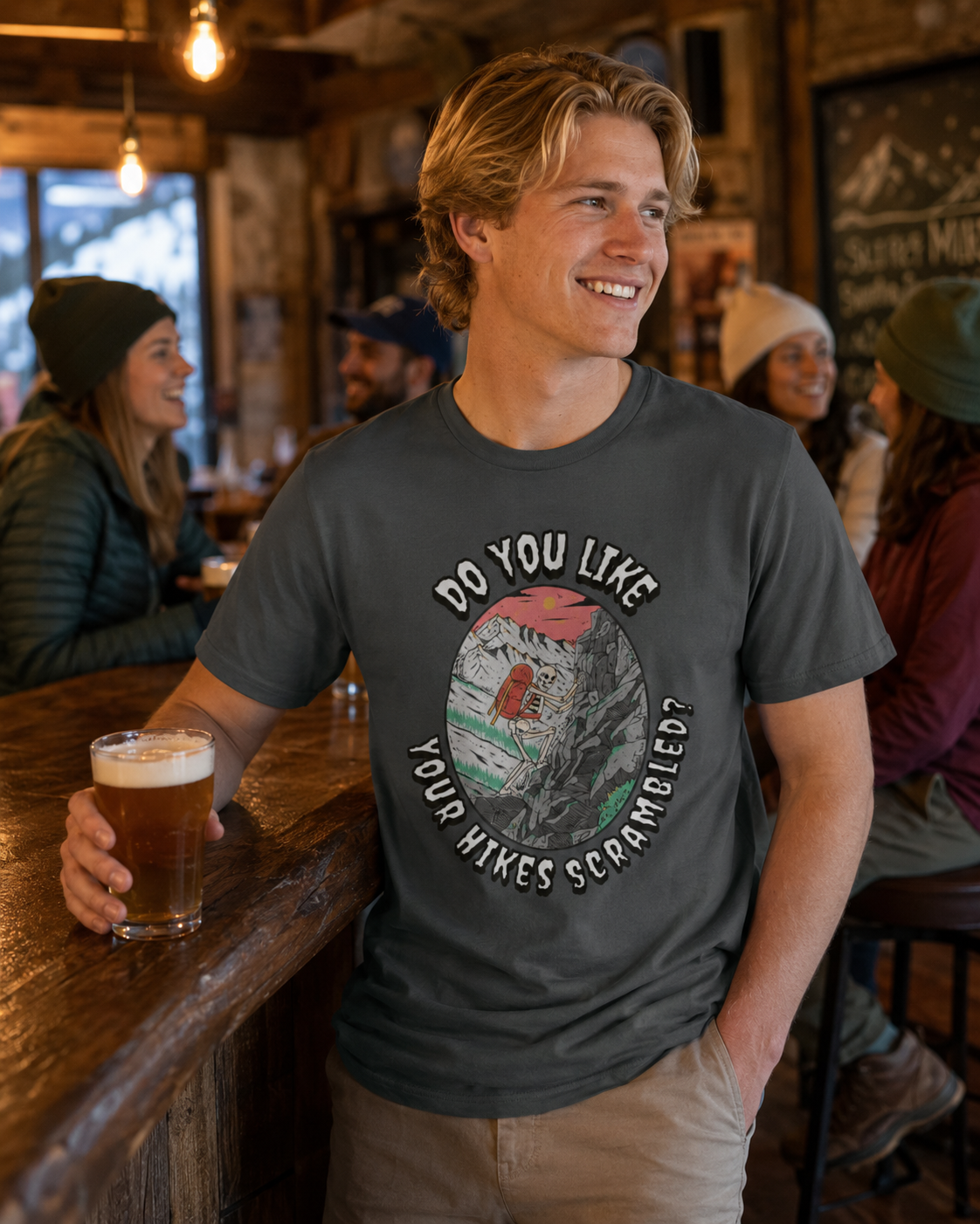 Man wearing a Deep Heather Do You Like Your Hikes Scrambled? T-shirt featuring the skeleton scrambling graphic at a casual bar