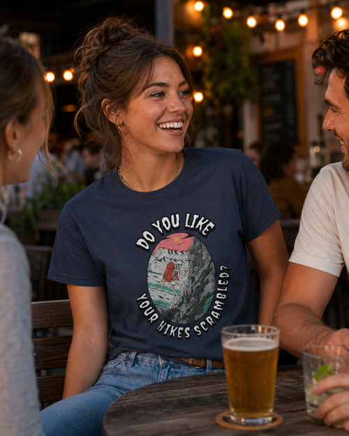 Woman wearing a Heather Navy Do You Like Your Hikes Scrambled? T-shirt featuring the skeleton scrambling graphic while having drinks at a bar