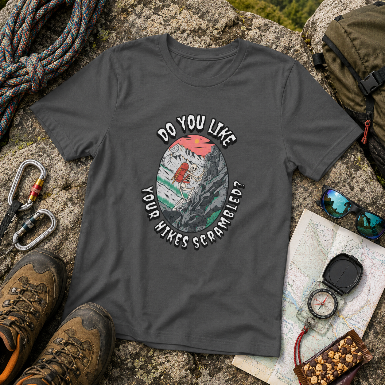 Deep Heather Do You Like Your Hikes Scrambled? T-shirt featuring a skeleton scrambling over rocks, flat lay with hiking and climbing gear